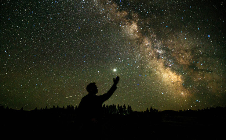 Photo of a figure silhouetted against the night sky, reaching up towards the stars